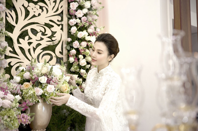 Người đẹp mặc áo dài gấm lụa trắng do nhà thiết kế Anh Thư làm riêng cho cô. Bộ lễ phục cưới được đính kết công phu, tinh xảo tôn vẻ đẹp sang trọng, quyến rũ cho cô dâu. Ngọc Duyên kiểm tra lại các khâu chuẩn bị ở nhà gái, trước khi nhà trai tới làm lễ xin dâu.